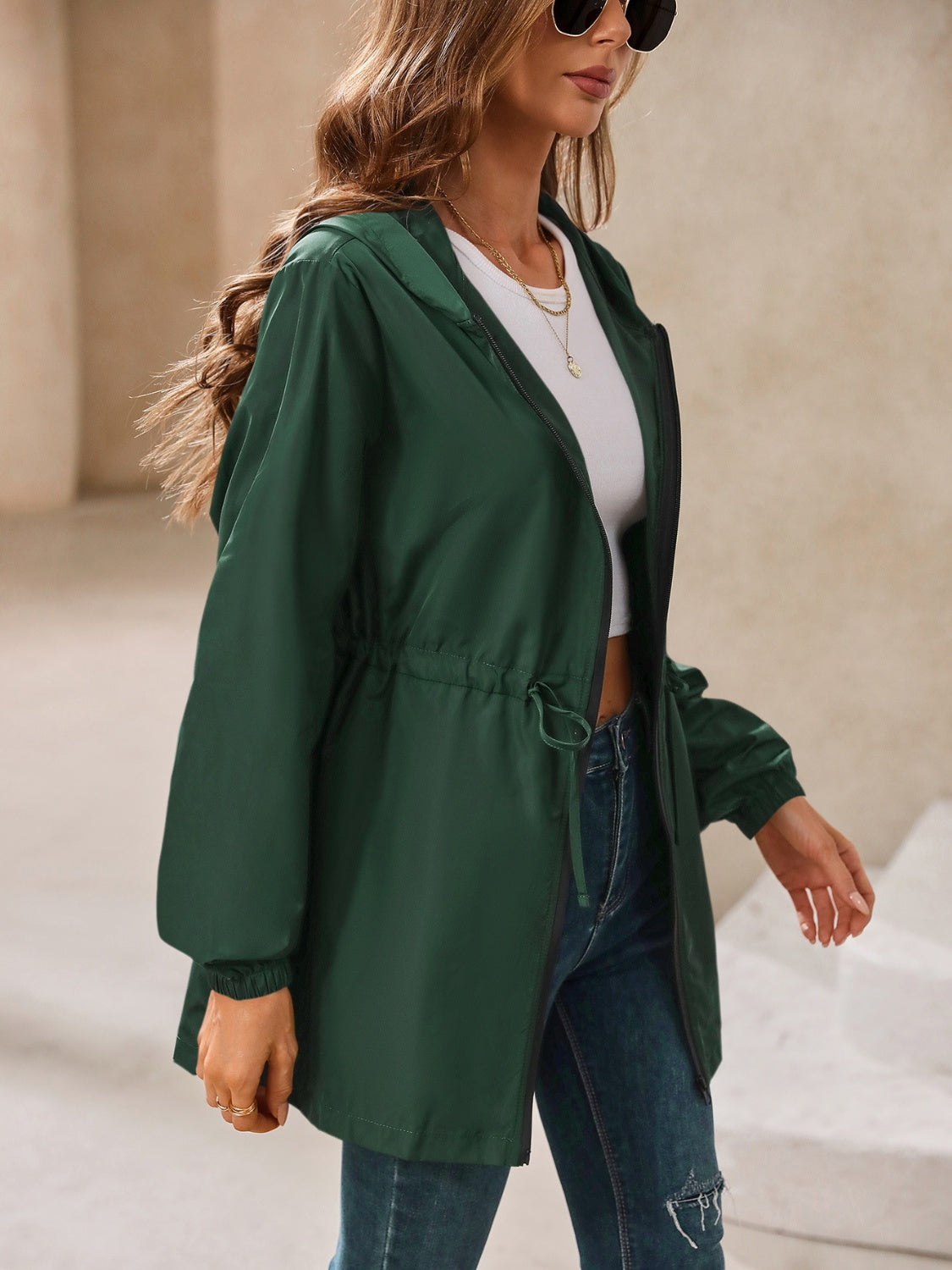Dark green hooded jacket with cinched waistline and zip front, styled with jeans.