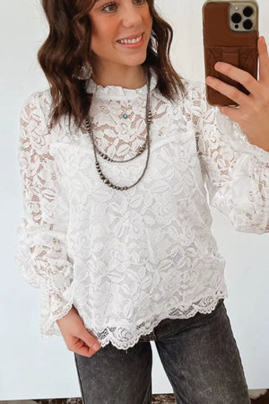 White lace blouse with ruffled neckline, long sleeves, and scalloped hem.