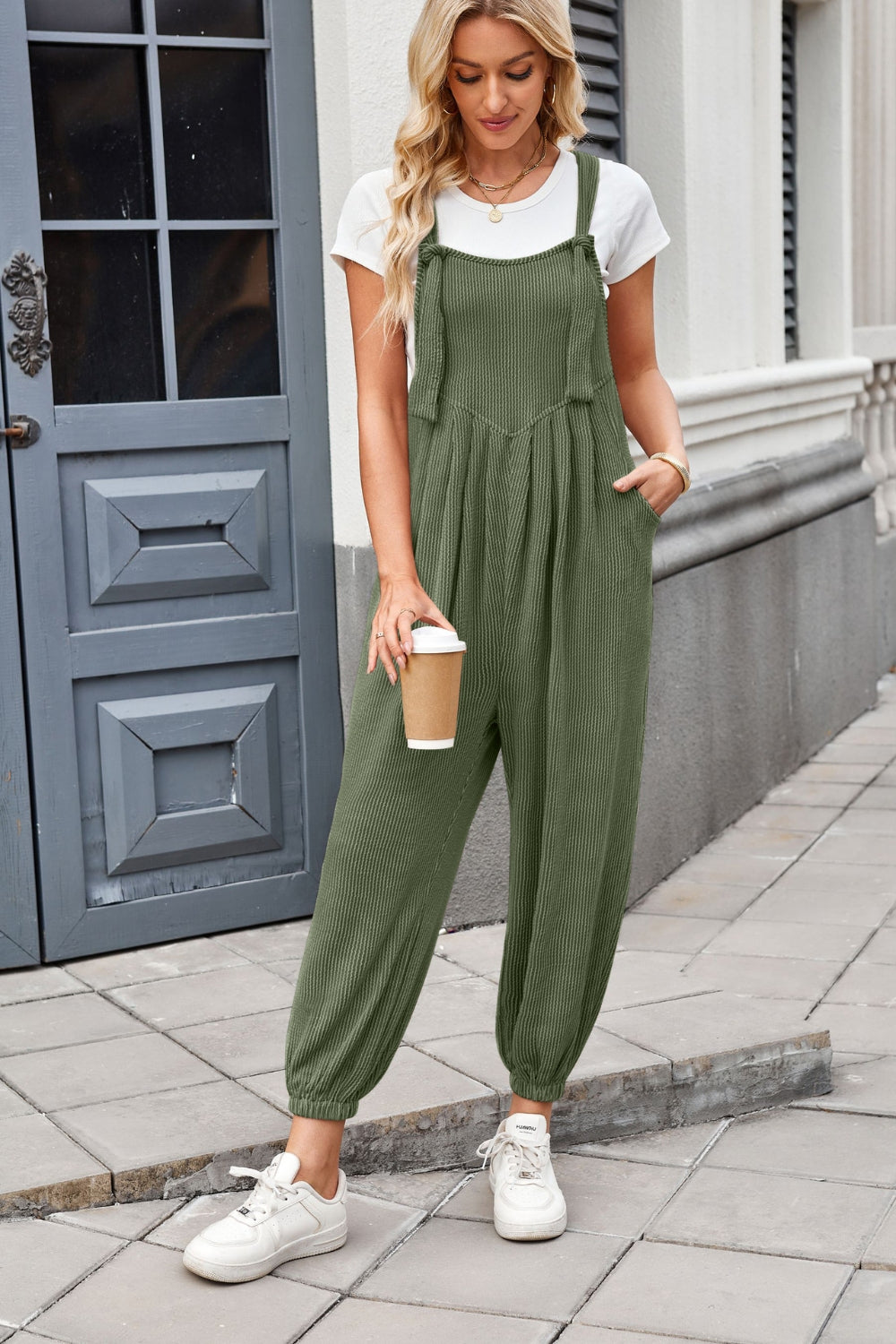 Olive green corduroy overalls with barrel legs and tie straps, worn with a white tee.