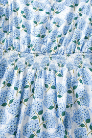 Midi dress with blue hydrangea print, smocked waist, and flutter sleeves.