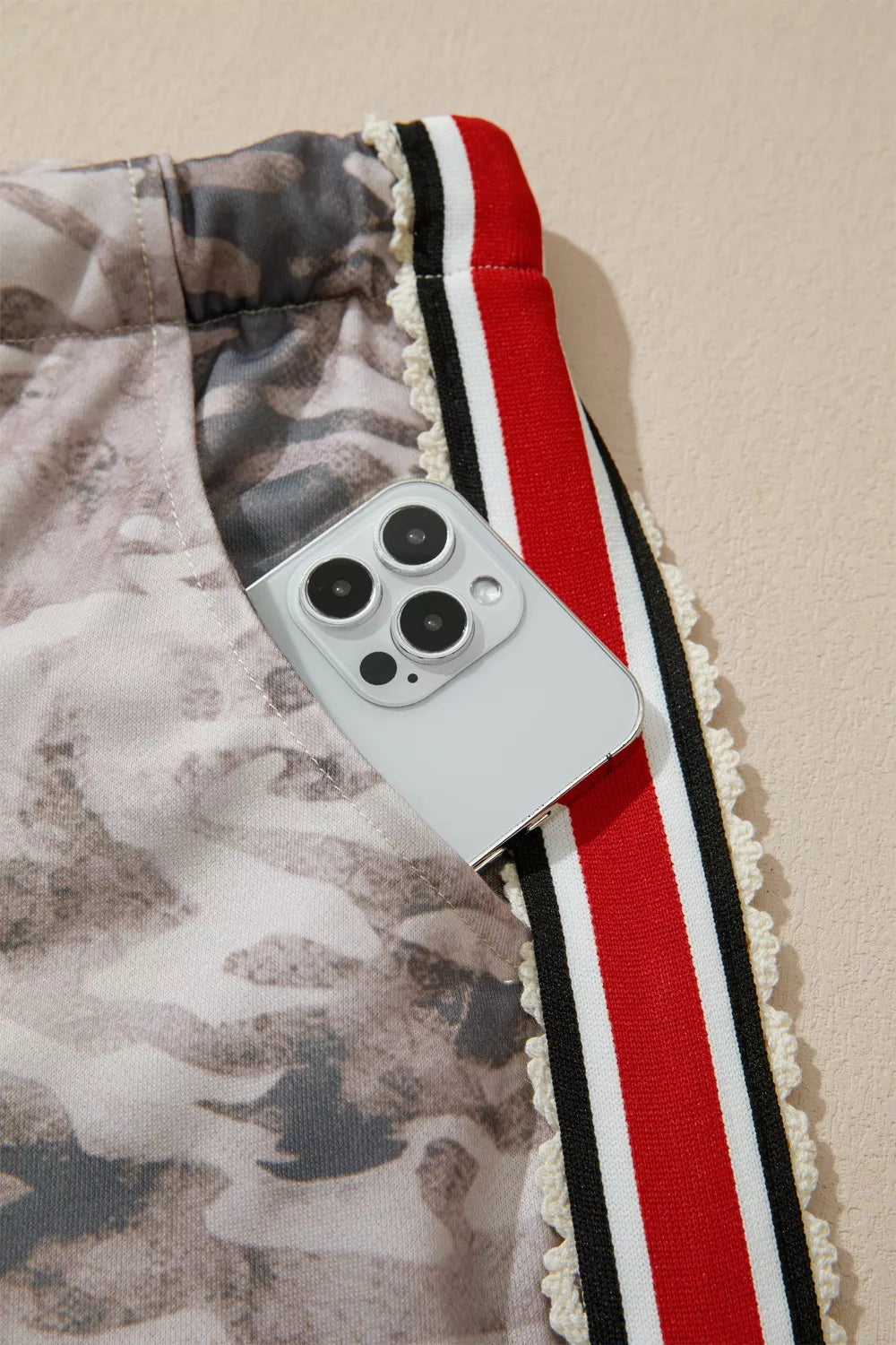 Camo print relaxed fit maternity pants with red, black, and white striped trim and a phone in the pocket.
