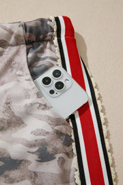 Camo print relaxed fit maternity pants with red, black, and white striped trim and a phone in the pocket.