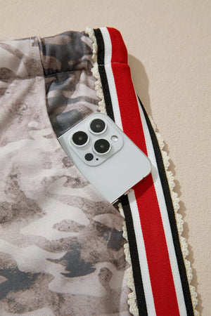 Camo print relaxed fit maternity pants with red, black, and white striped trim and a phone in the pocket.