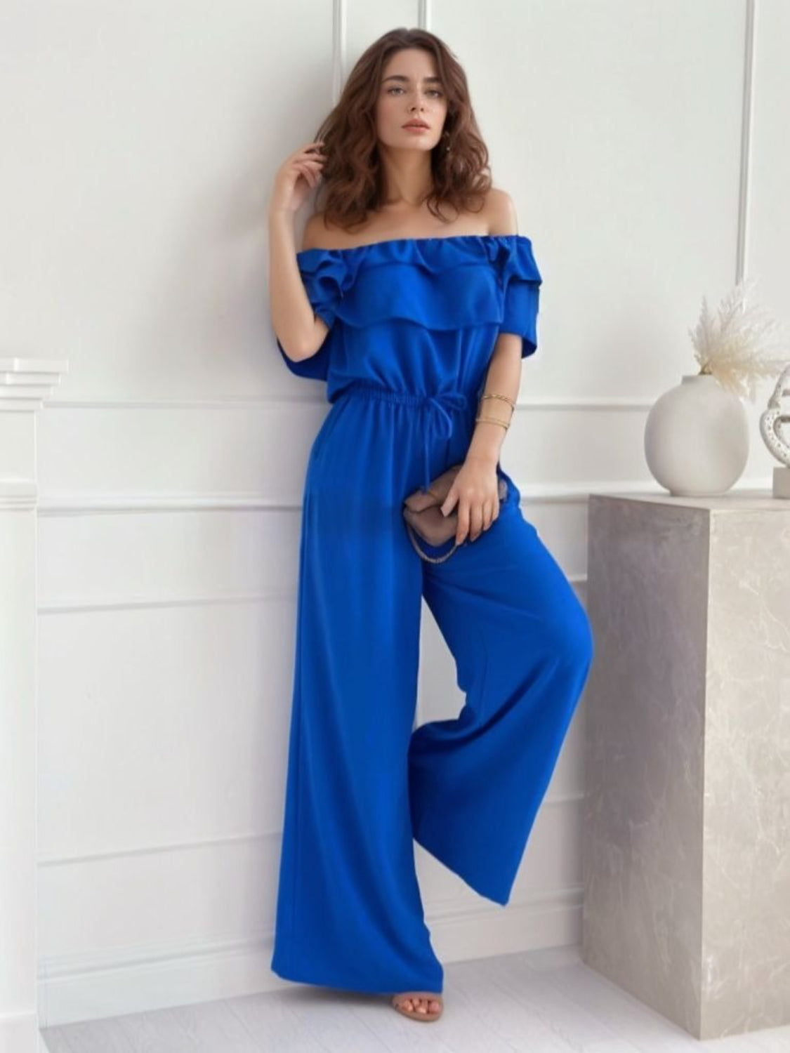 Royal blue off-the-shoulder jumpsuit with ruffle detail and wide legs.