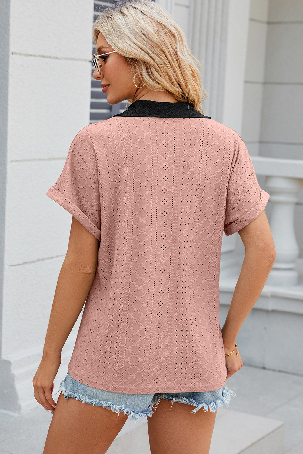 Blush pink perforated polo top with black collar and cuffed short sleeves.