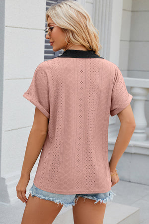 Blush pink perforated polo top with black collar and cuffed short sleeves.