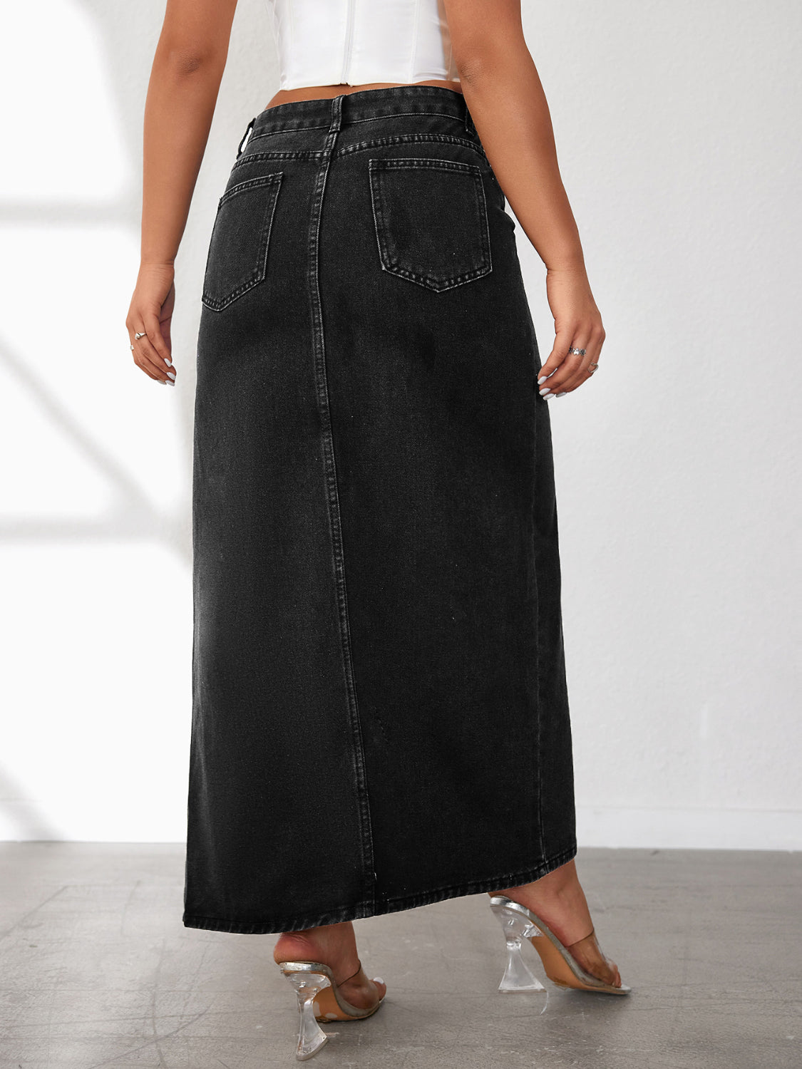 Black washed denim maxi skirt with a high slit, featuring back pockets and a center seam.
