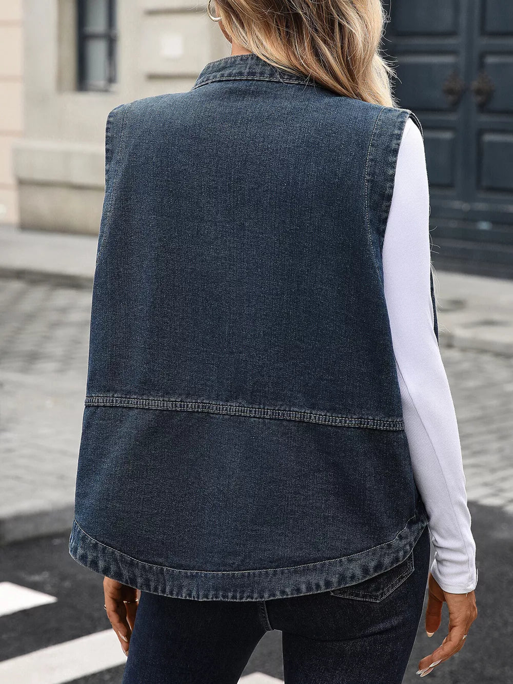 Washed black denim vest with band collar and curved hem, styled over a white long-sleeve top.