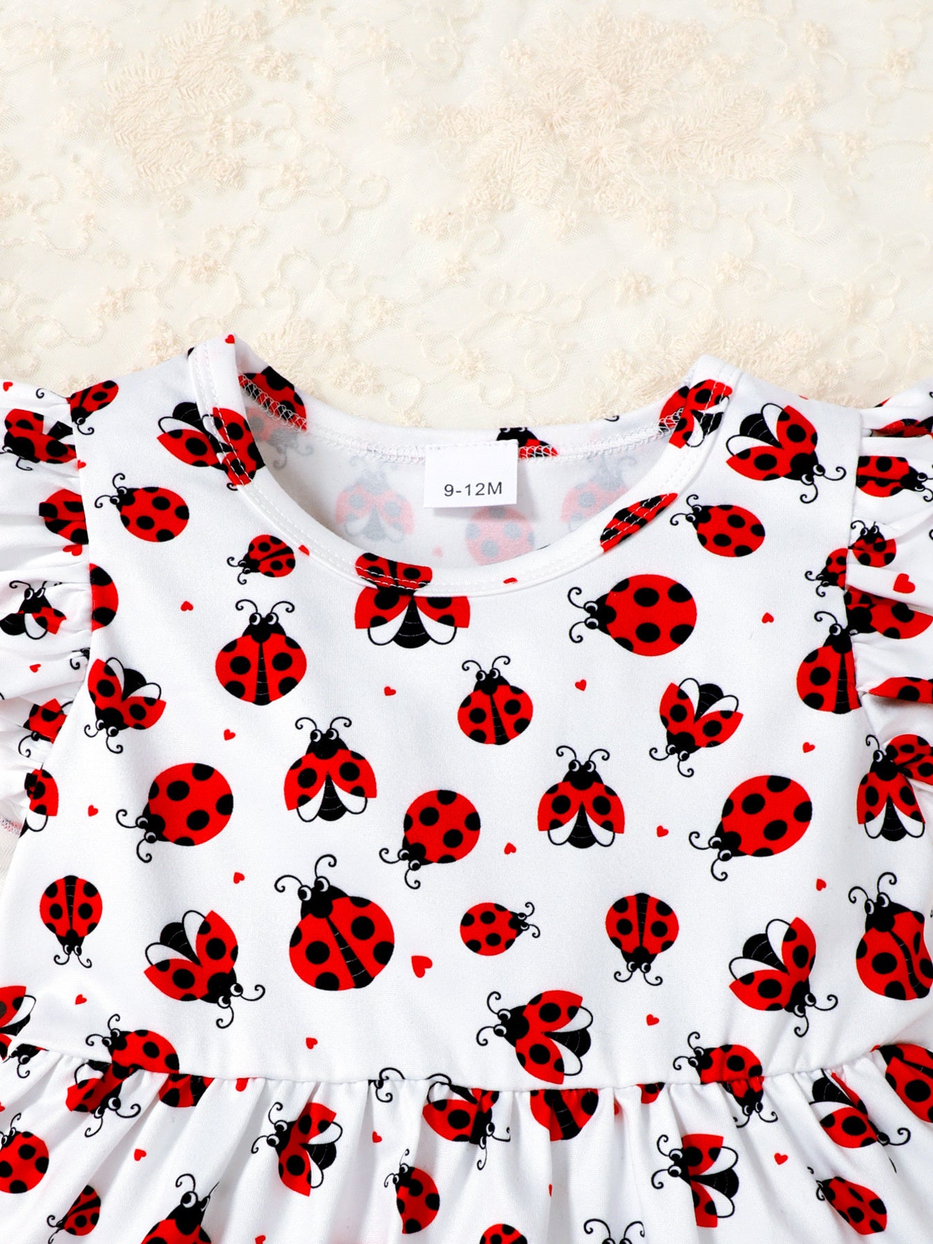 Baby set with white fabric, red ladybug print, and ruffle trim sleeves.