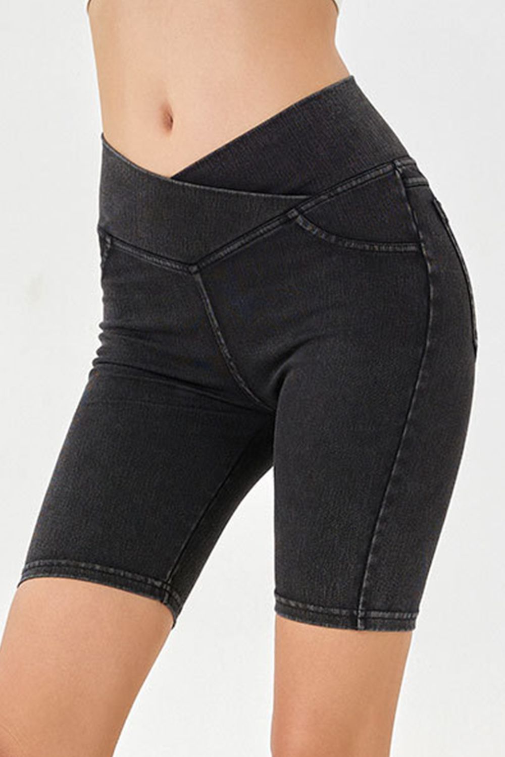 Black denim bermuda shorts with a crisscross waistband and asymmetrical detail.