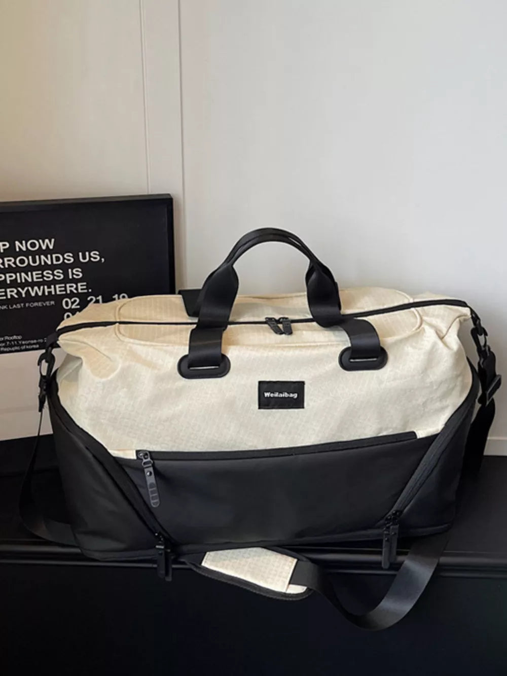 Textured two-tone large duffle bag in cream and black with adjustable strap and zip pockets.