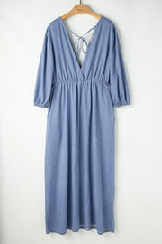 Light denim maxi dress with V-neck, cinched waist, puff sleeves, and tie-back detail.