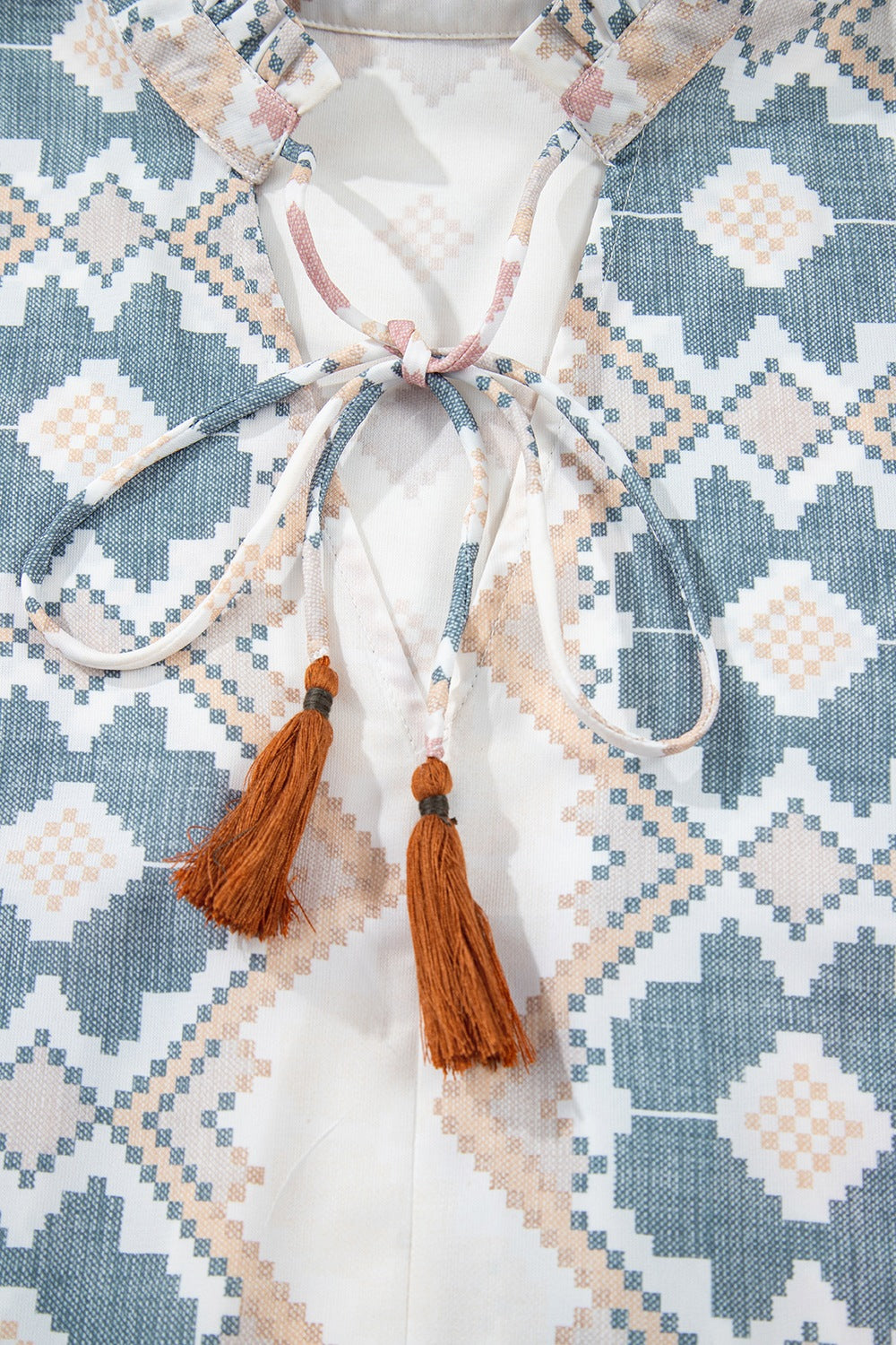 Geometric print blouse with tassel tie detail and ruffled collar.