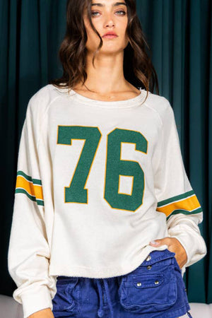 White raglan sleeve sweatshirt with green and gold '76' graphic and sleeve stripes.