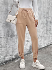 Beige joggers with drawstring waist and tapered hemline, styled with white sneakers.