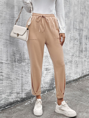 Beige joggers with drawstring waist and tapered hemline, styled with white sneakers.