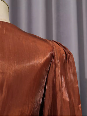 Brown metallic maxi dress with ruched shoulder detail and draped skirt slit.