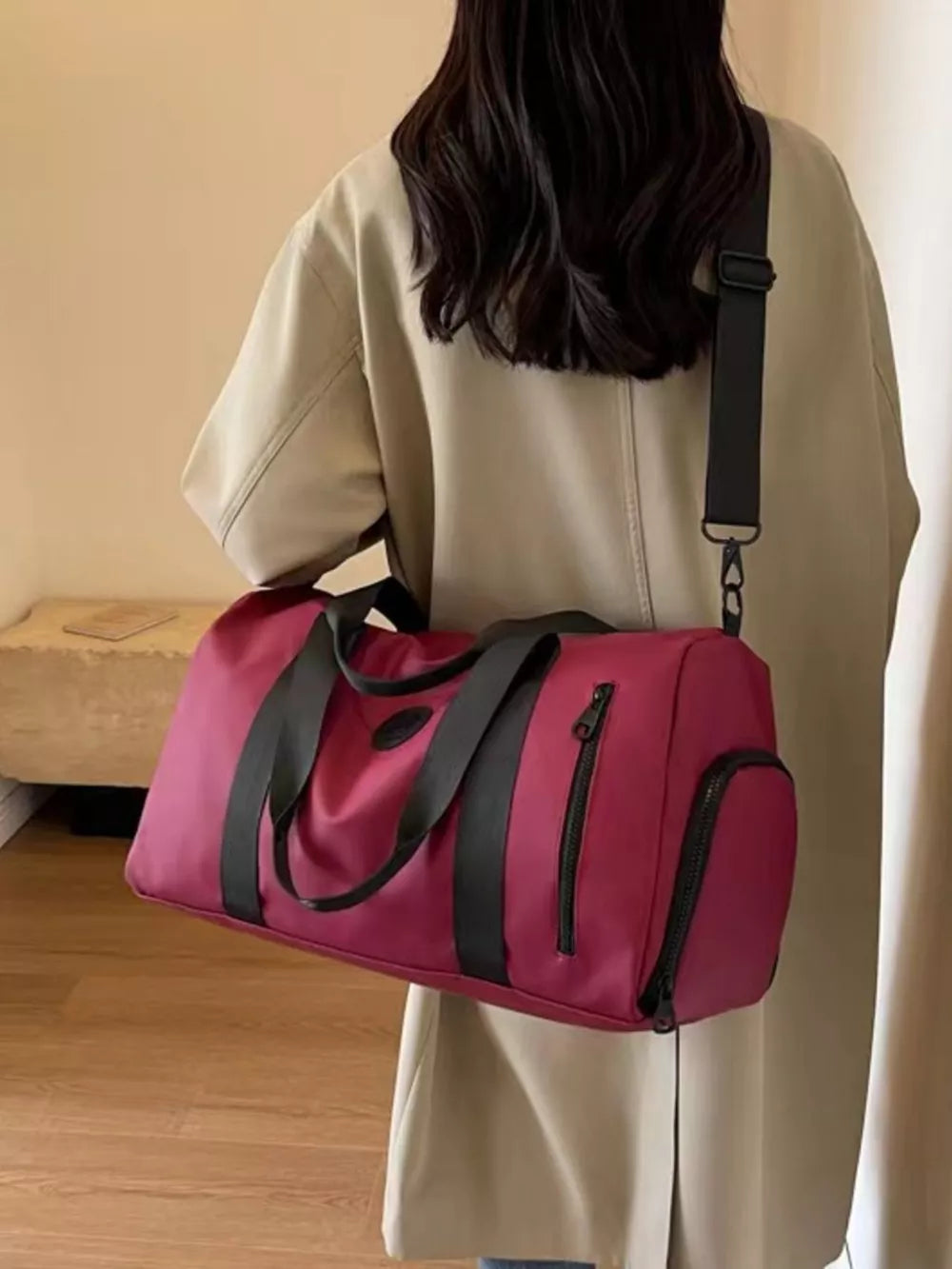 Wine red travel bag with black straps and zippers, worn over the shoulder.