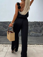 Black wide-leg maternity jumpsuit with floral applique on one shoulder.
