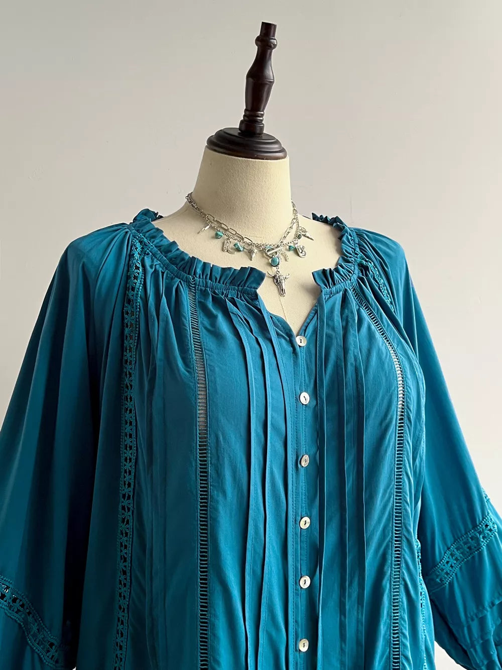Teal ruffled lantern sleeve pleated blouse with button-down front and cutout details.