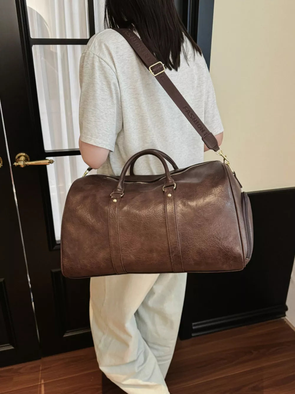Brown pu leather travel bag with detachable strap and top handles, worn crossbody.