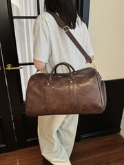 Brown pu leather travel bag with detachable strap and top handles, worn crossbody.