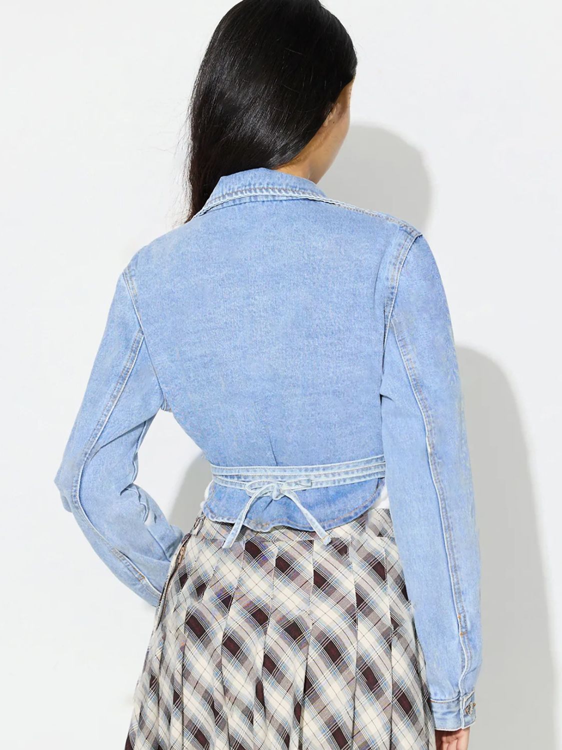 Medium wash denim wrap jacket with tie waist detail and asymmetric cut.