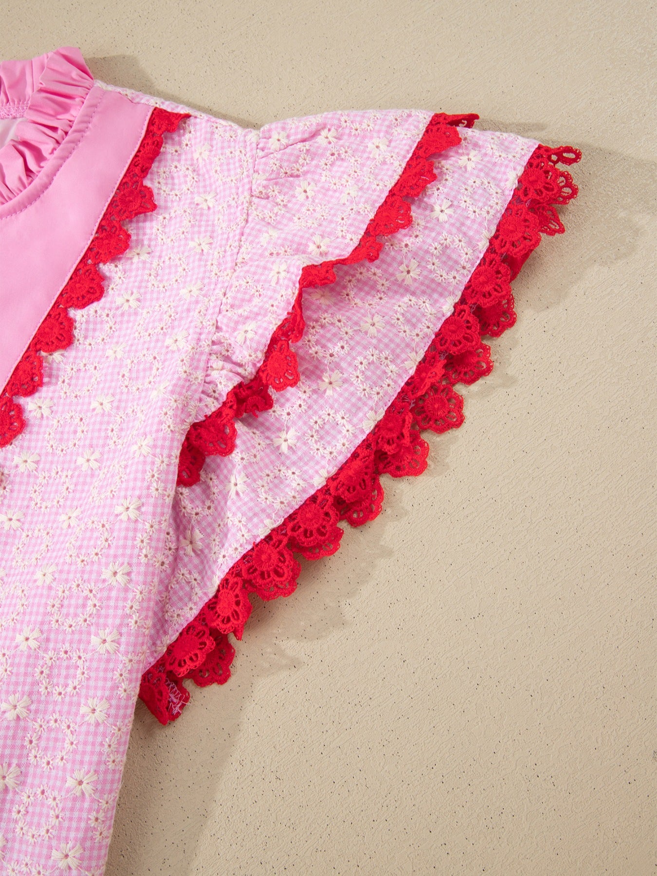 Pink eyelet embroidered blouse with flutter sleeves and red lace trim.