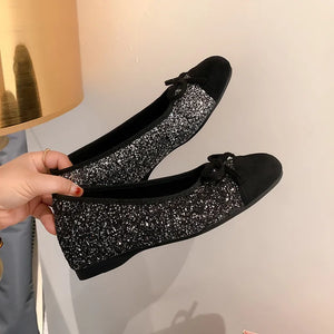 Black glitter ballet flats with black suede cap toes and bows.