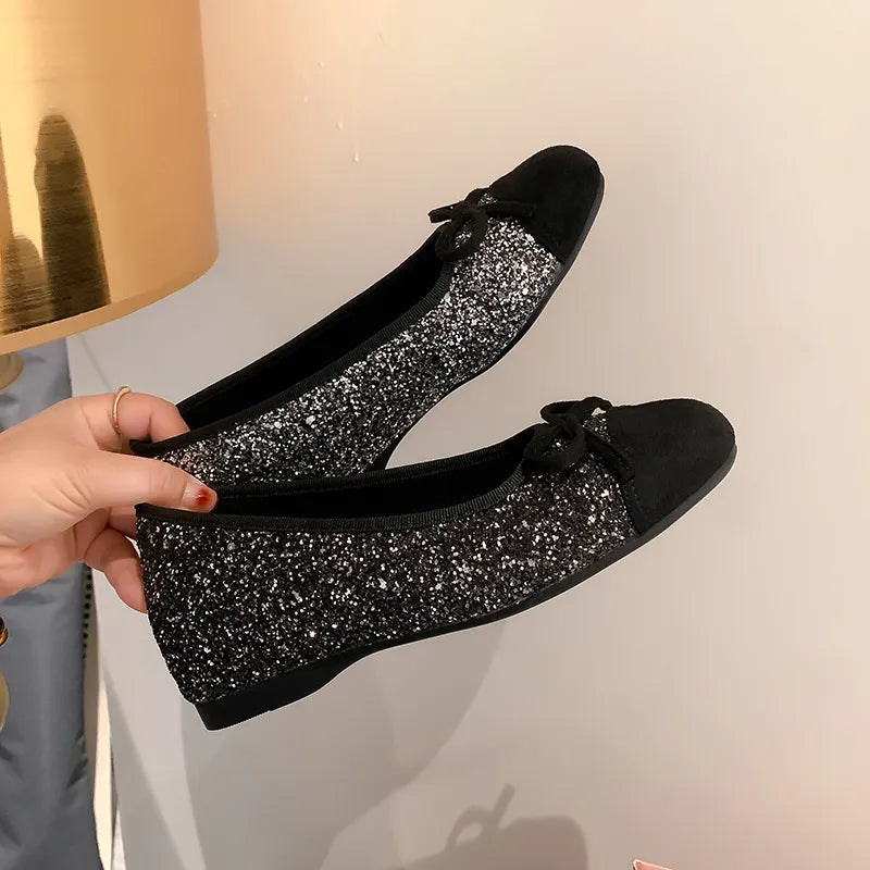 Black glitter ballet flats with black suede cap toes and bows.