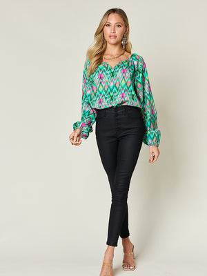 Green ikat print blouse with voluminous sleeves and V-neck, styled with black pants.