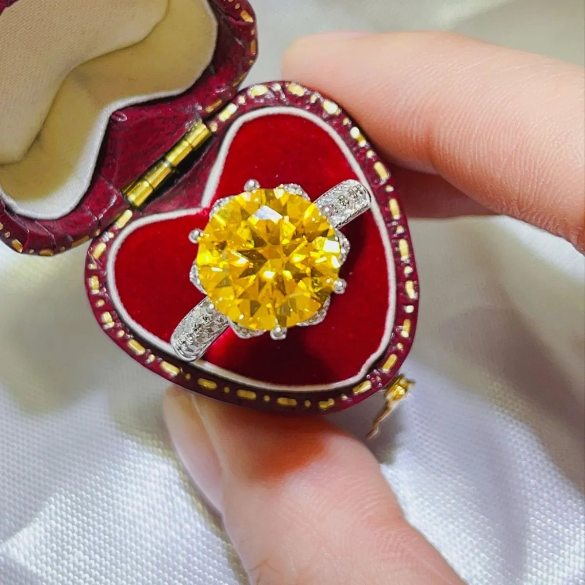 Radiant canary moissanite solitaire ring with diamond band in a heart-shaped box.