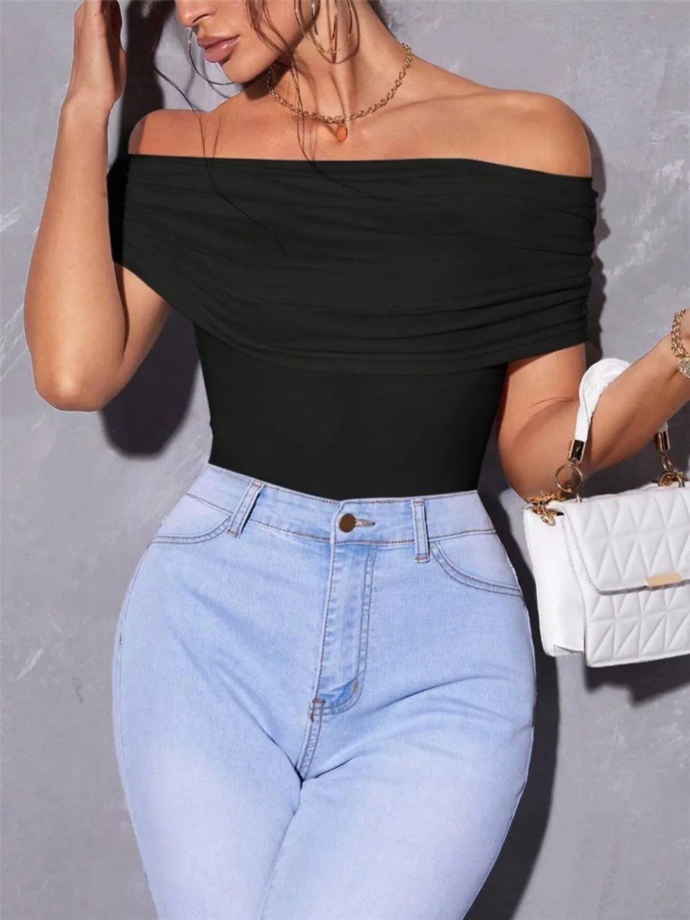Black off-shoulder ruched t-shirt with short sleeves, styled with light wash jeans.