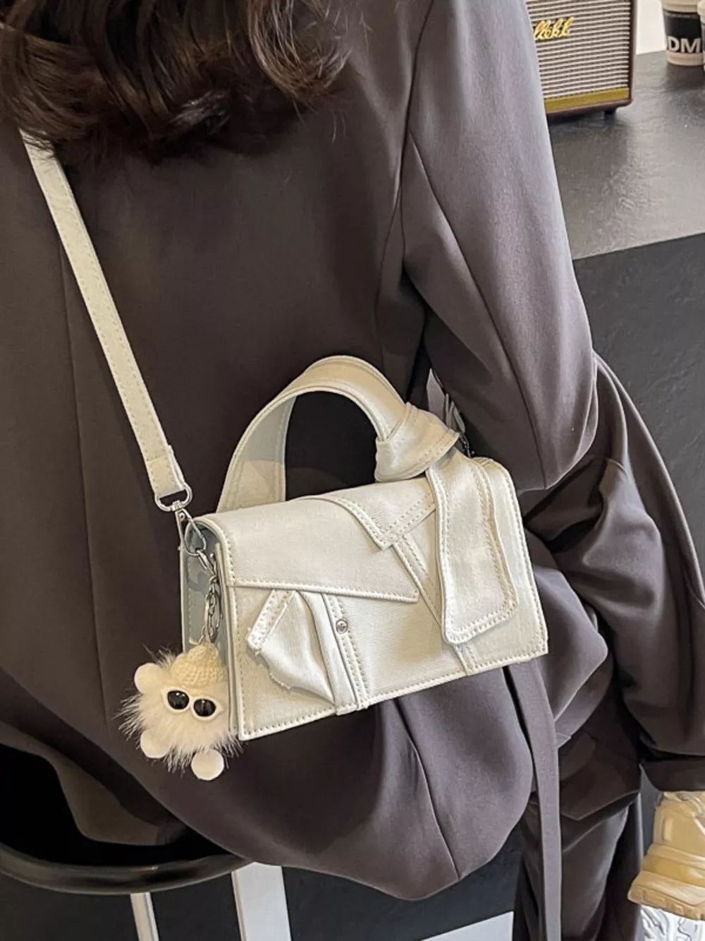 Artisanal mini denim crossbody bag in off-white with a fuzzy charm and adjustable strap.