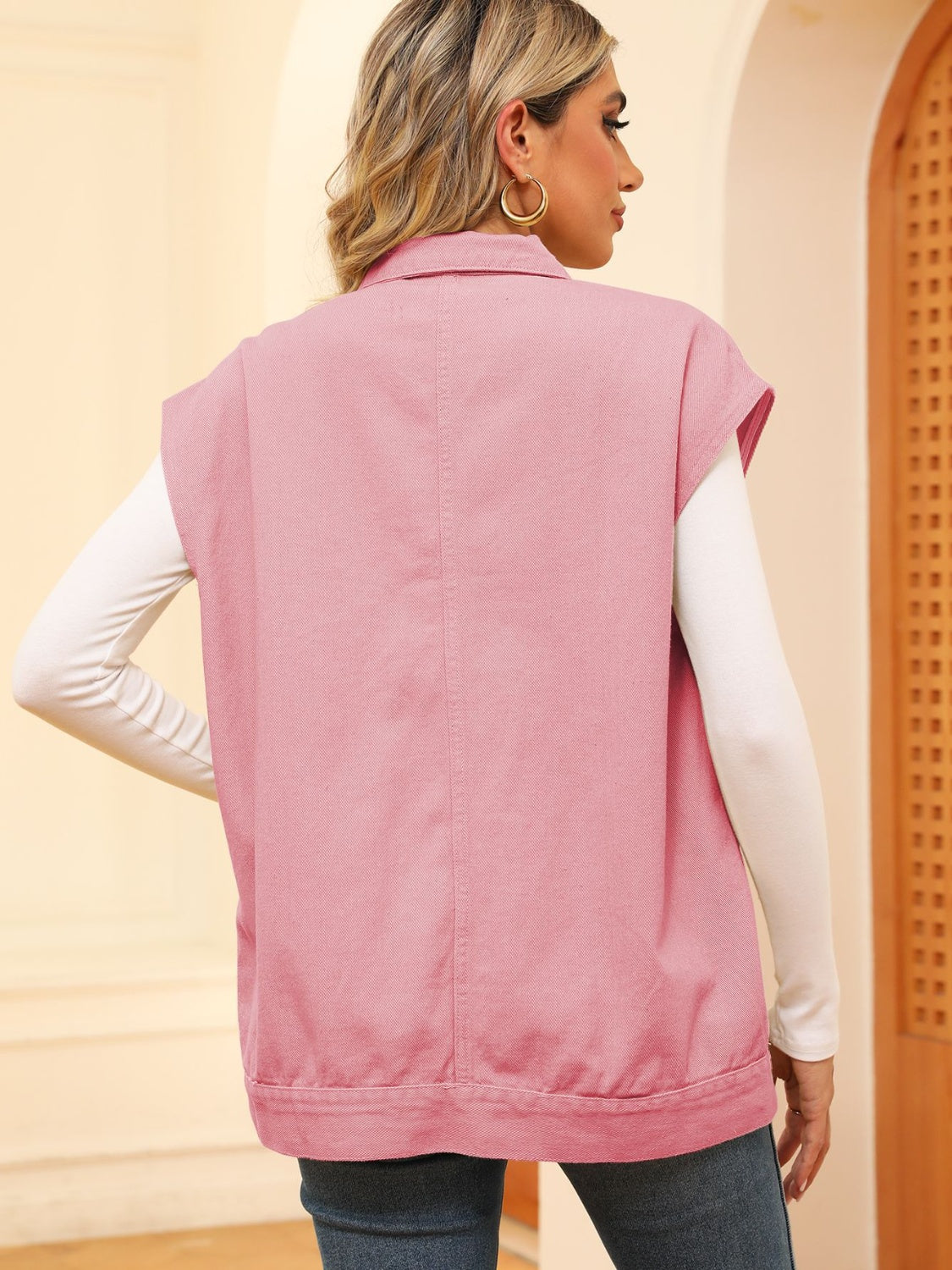 Pink utility denim vest with collar and buttoned front, worn over a white long-sleeve shirt.