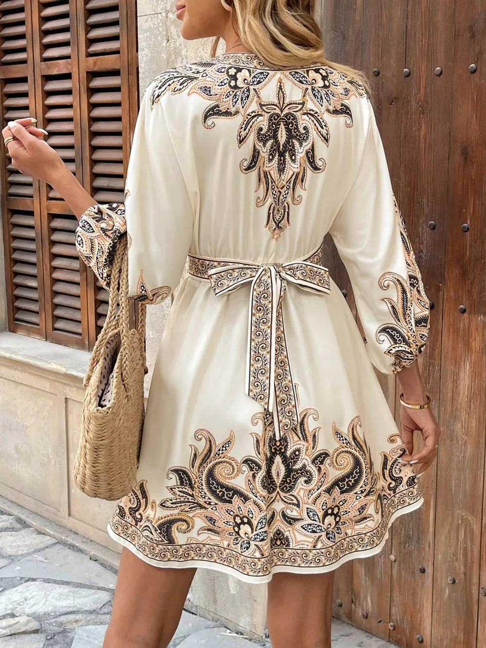 Cream mini dress with vibrant paisley print, tie waist, and billowy sleeves.
