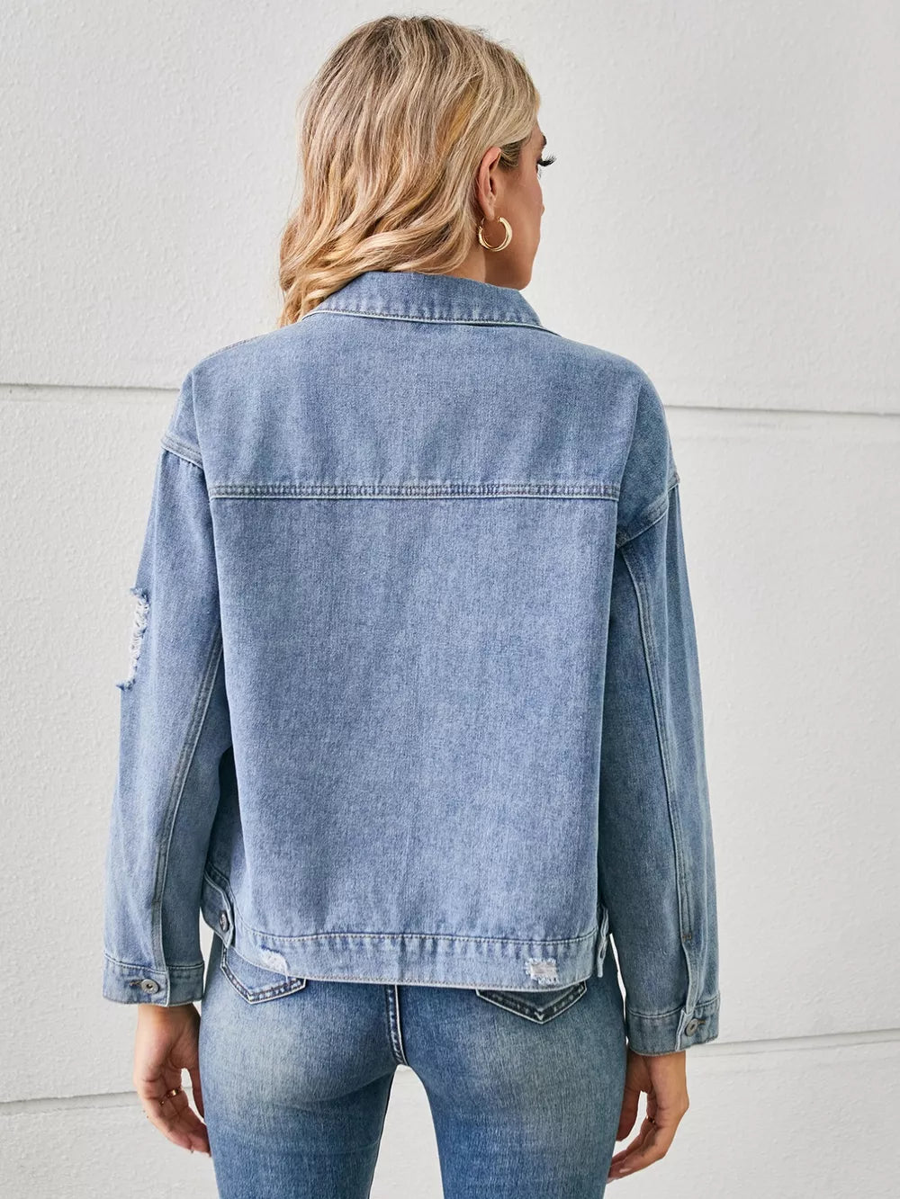 Light wash denim trucker jacket with distressed details and button cuffs.