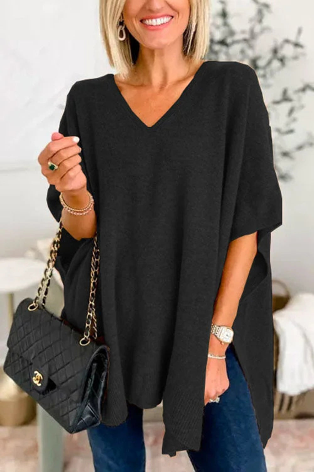 Black knit V-neck poncho top with relaxed fit and side slits, styled with a quilted handbag.
