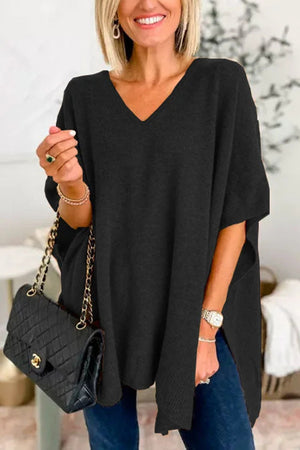 Black knit V-neck poncho top with relaxed fit and side slits, styled with a quilted handbag.