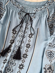 Light blue embroidered tie neck blouse with tassels and peasant sleeves.