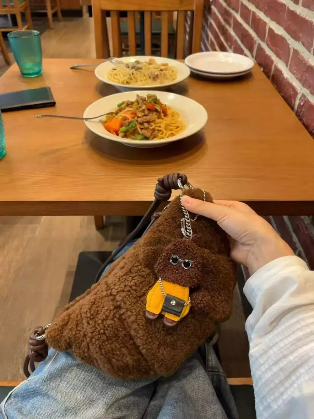 Brown plush crossbody bag with knot strap and dog charm accessory.