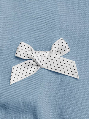 Chic buttoned vest and tailored shorts set detail: white polka dot ribbon bow on blue fabric.