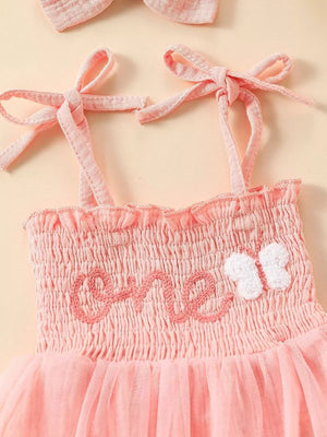 Pink smocked baby bodysuit with embroidered 'one' and butterfly detail, plus matching headband.