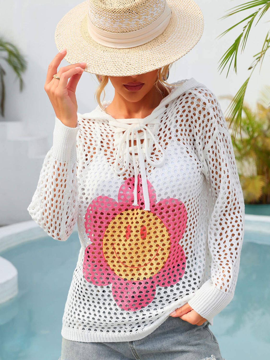 White knit hoodie with lace-up neckline and smiley flower graphic.