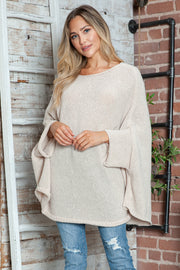 Cream knit sweater with relaxed cape sleeves and boat neck, styled with jeans.