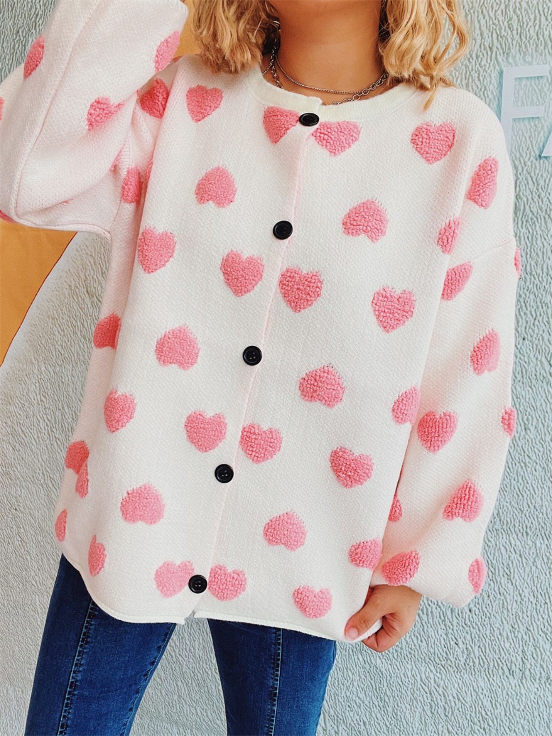 Textured white acrylic button-down cardigan with pink heart motifs and black buttons.