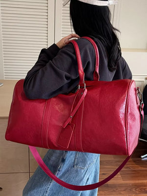 Textured metallic duffle bag in wine red with top handles and detachable strap.