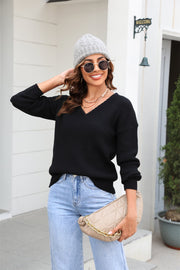 Black ribbed knit v-neck sweater with long sleeves, styled with jeans and a beanie.