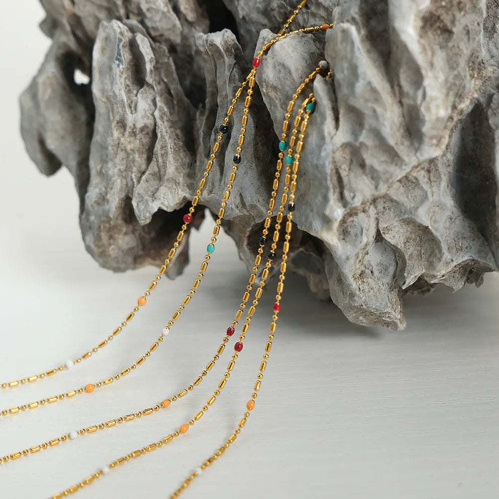 Gold necklaces with colorful beads and gold bar accents cascade down, featuring red, black, white, orange, and turquoise