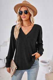Black V-neck long sleeve top with button cuffs, styled with jeans and a clutch